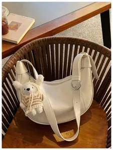 Chic creamy white crescent crossbody bag featuring a cute plush bunny charm detail