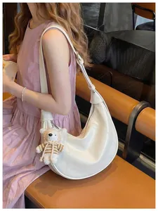 Elegant white crescent dumpling crossbody bag with cute knitted bear charm accessory.