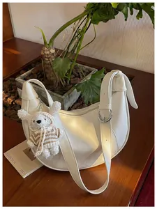 Minimalist white crescent shoulder bag featuring a cute bear charm and knot strap detail