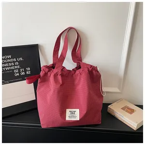 Close-up of large maroon grid canvas tote bag with drawstring detail and brand patch