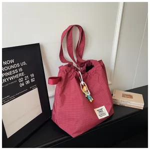 Lifestyle shot of a large red checkered tote bag featuring a decorative pearl charm.