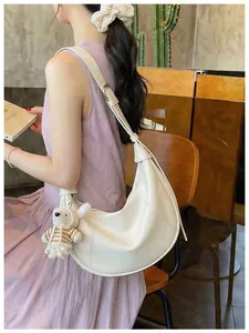 Detailed side view of a white hobo crescent bag with a bear pendant worn by a model.