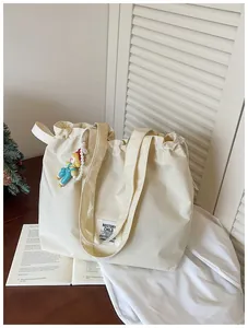Detail view of a cream-white grid canvas tote bag with a drawstring and doll pendant