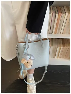 Light blue textured leather tote bag with a cute teddy bear charm held by a person