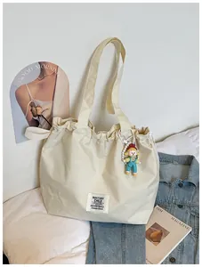 Cream canvas tote bag detail featuring a unique drawstring design and cute doll keychain