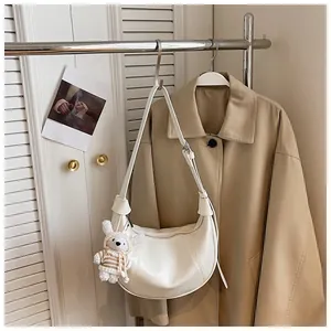Detail view of white crescent hobo shoulder bag with a cute bear charm hanging on a tan trench coat