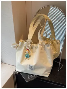 Macro view of a cream grid-textured tote bag featuring a cute cartoon doll charm.