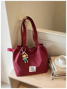 Lifestyle detail of a red checkered canvas tote bag featuring a cute doll charm and patch