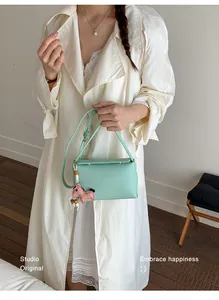 Primo piano della borsa a tracolla verde menta con ciondolo rosa tenuta da una modella