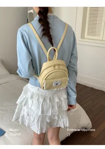 Detailed rear view of a cute yellow mini backpack with a bear patch and lace trim