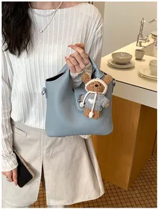 Detailansicht einer hellblauen Eimertasche aus Leder mit einem süßen Bärenanhänger.