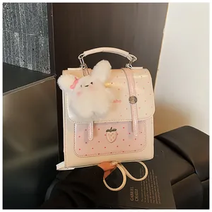 Detail view of a white polka dot backpack with a strawberry patch and plush bunny charm