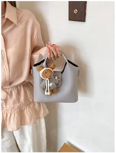 Nahaufnahme einer grauen Eimertasche aus Kieselleder mit einem süßen Bärenanhänger