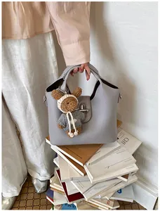Graue Handtasche aus genarbtem Leder mit süßem Plüschbären auf Büchern