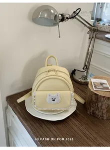 Detail showing cream mini backpack with cute cartoon bear patch and lace trim