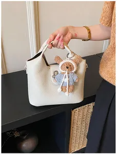 Detail einer cremeweißen Eimertasche aus Kieselleder mit niedlichem Teddybär-Anhänger