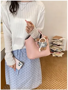Elegante rosa Leder-Eimertasche mit süßem Bärenanhänger an einem Model getragen.