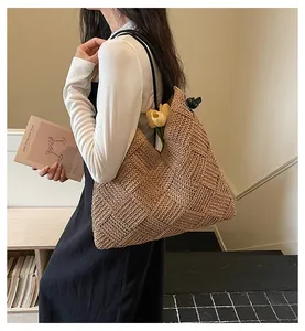 Vue détaillée d'un grand sac fourre-tout en paille naturelle tissée porté par un mannequin.