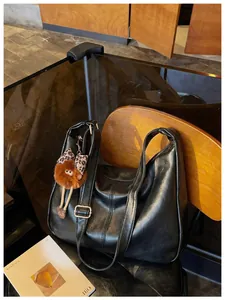 Large black faux leather hobo tote bag with fuzzy charm on a vintage wooden chair