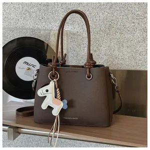 Close-up of a stylish brown textured handbag with a cute horse charm on a wooden shelf.