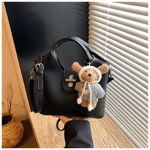 Detailaufnahme einer schwarzen Eimertasche aus Leder mit einem süßen Bärenanhänger. (83 chars)