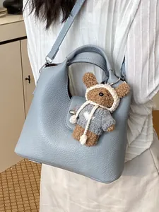 Elegante hellblaue Ledereimertasche mit feiner Narbung, süßem Bärenanhänger und Schultergurt.