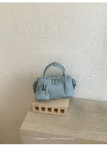 Detail of a light blue litchi grain bowling bag on a minimalist stone pedestal.