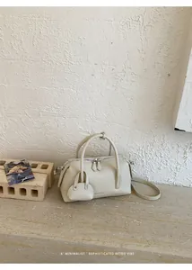 Minimalist cream litchi grain bowling bag with matching mini pouch accessory detail.