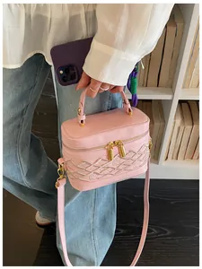 Bolso mini rosa tipo caja con detalle trenzado sostenido por una persona con ropa casual
