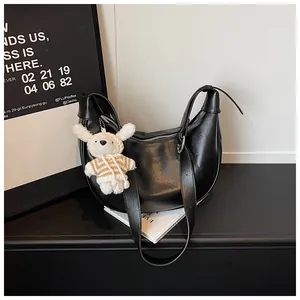 Chic black crescent dumpling bag with a cute plush rabbit charm on a minimalist desk.