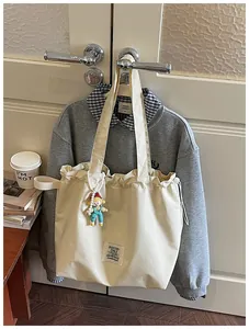Detailed view of cream canvas tote bag with doll charm hanging in a lifestyle setting