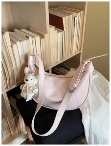 Pink crescent crossbody bag with cute knitted bear charm on a wooden shelf setting