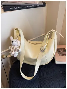 Cream crescent dumpling bag with cute bear keychain accessory in lifestyle setting.