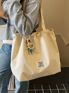 Stylish large capacity beige canvas tote bag with cute doll pendant for casual commuting