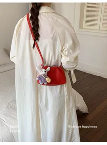 Modelo con vestido blanco muestra bolso bandolera de cuero rojo con detalle de conejo de peluche