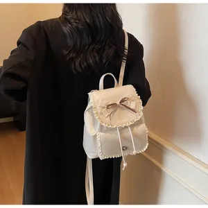 Detail of cream white backpack with lace edges and bow detail on female model.