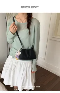 Bolso bandolera negro tipo nube con lindo colgante de osito en una escena de estilo de vida real.