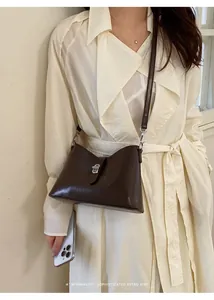 Primo piano di una borsa a tracolla marrone abbinata a un elegante trench coat bianco panna.