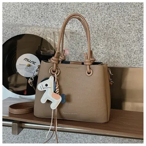 Close-up detail of an elegant khaki textured leather bucket bag with horse charm