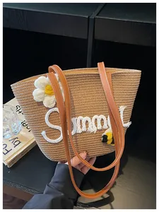 Detailed view of woven straw bucket bag with white flower and Summer embroidery.