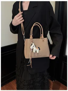 Stylish khaki textured handbag with white horse charm accessory on black blazer outfit