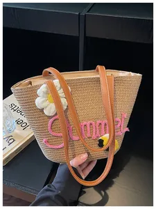 Detail of woven straw tote bag featuring pink Summer embroidery and flower charm