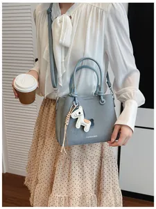 Close-up of stylish grey bucket bag with horse charm held by model in chic outfit.