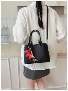 Detailed view of the black leather bucket bag with a red horse charm and tassel accessory.
