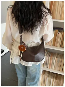 Elegant brown vegan leather crescent crossbody bag shown in a cozy library setting.