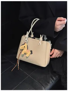 Close-up of a stylish cream bucket bag featuring a cute horse charm and knotted handles