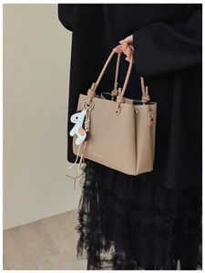Close-up detail of a beige fashion bucket bag being held by a model in a black outfit