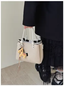 Detail of a stylish beige bucket bag featuring a cute horse charm and knotted handles