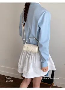 Detail of a cream mini cylinder crossbody bag with a lace heart patch and top handle