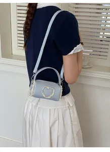Mini cylindrical light blue handbag with heart lace detail shown on a model's shoulder